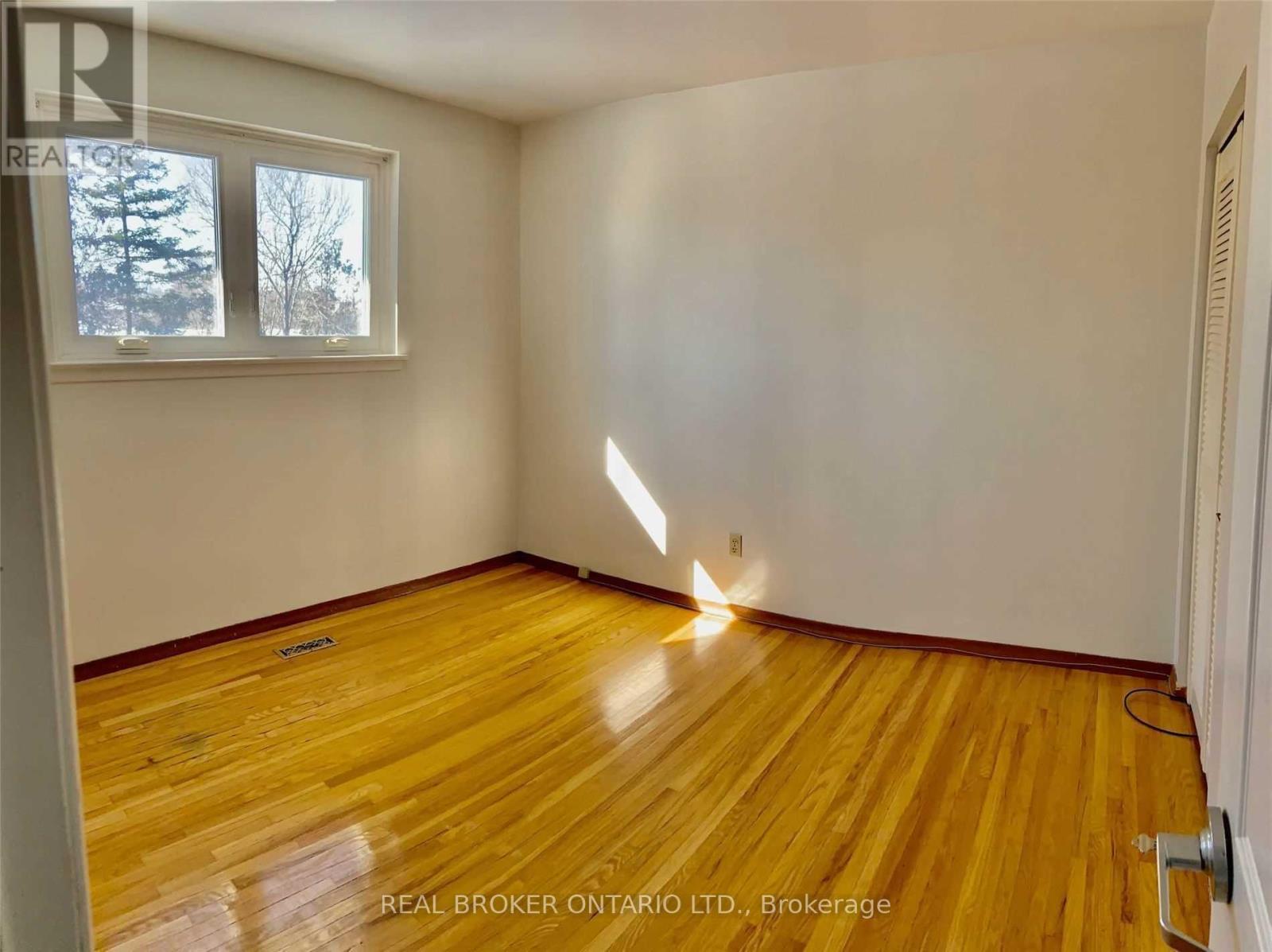 A room with wooden flooring and a window showing trees outside.