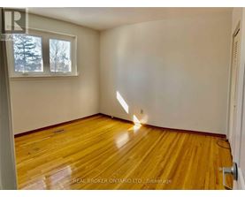 A room with wooden flooring and a window showing trees outside.