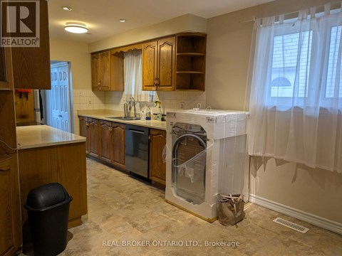 A kitchen with wooden cabinets and a black trash can.