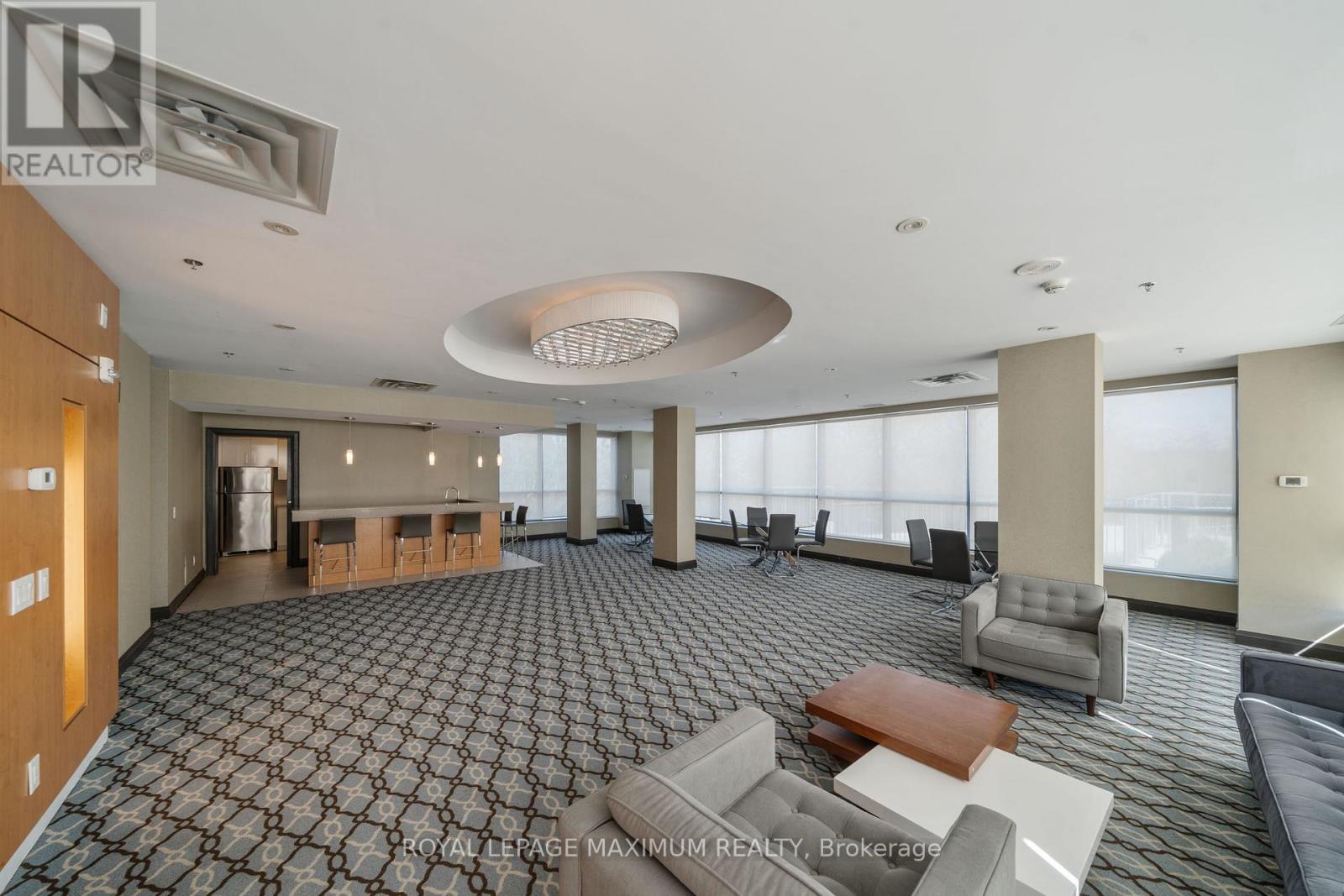 A spacious living room with a patterned carpet and a large circular light fixture on the ceiling.