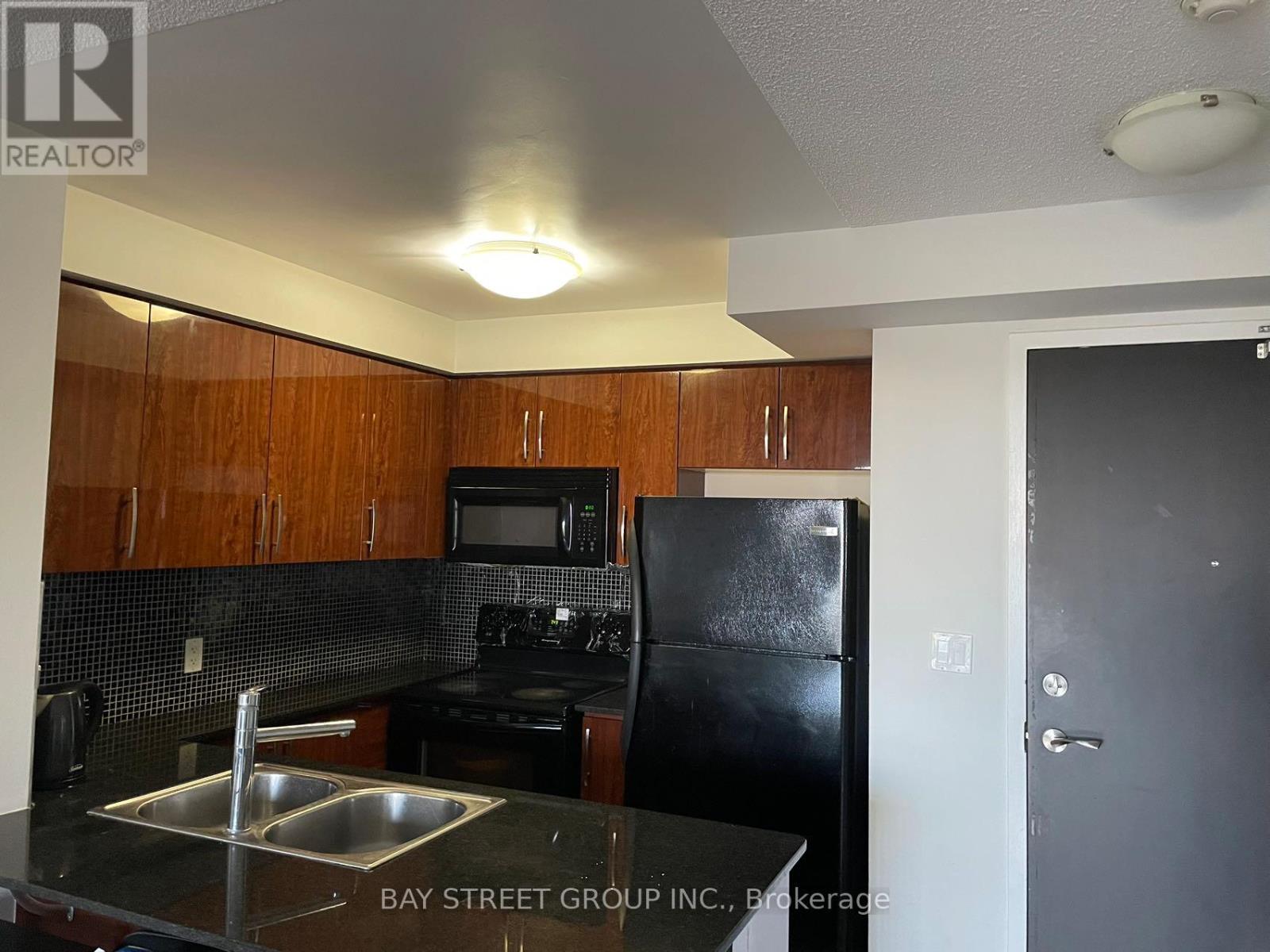 A kitchen with a black refrigerator and wooden cabinets.