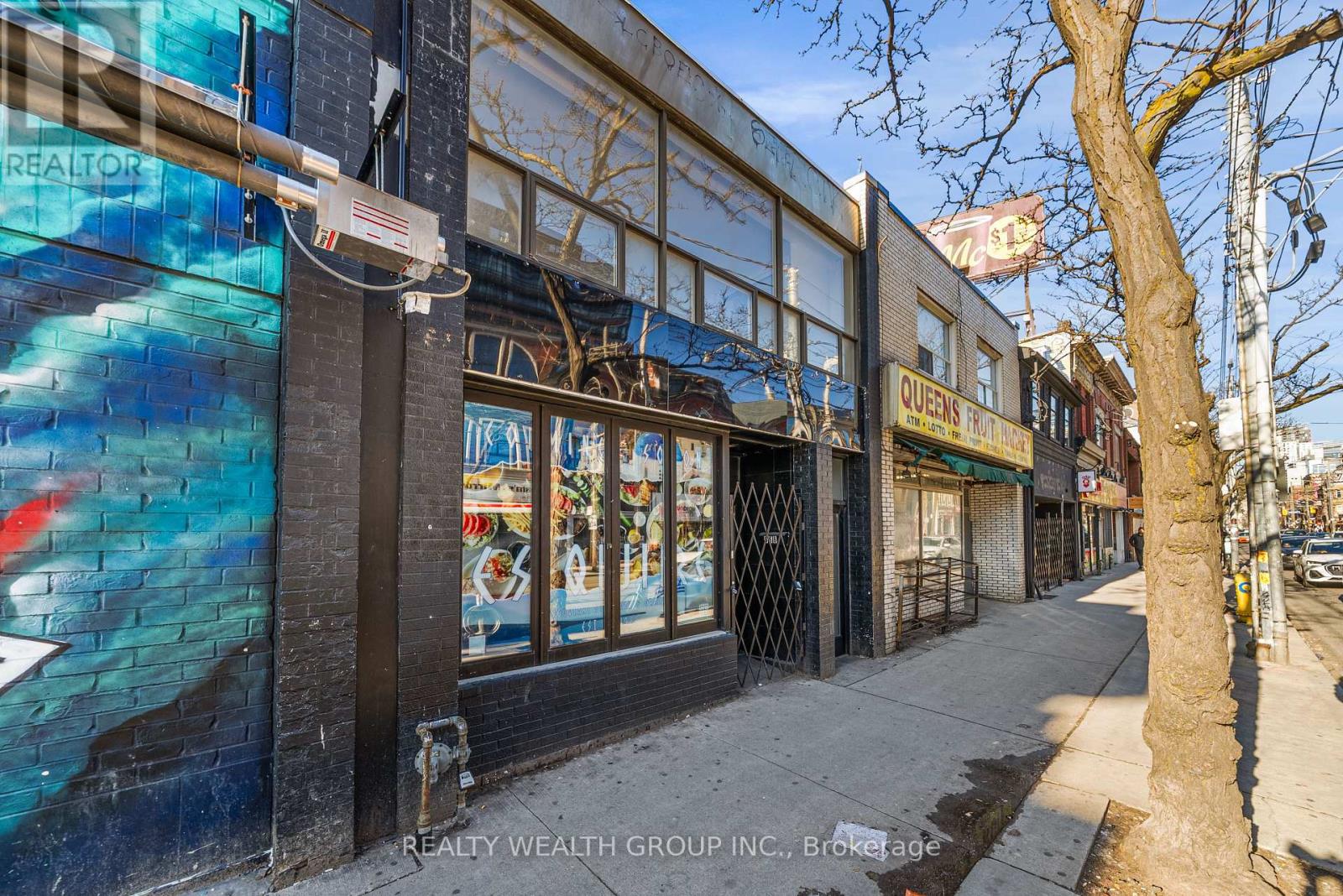 A street view of a building with a mural on the side and a tree in front.