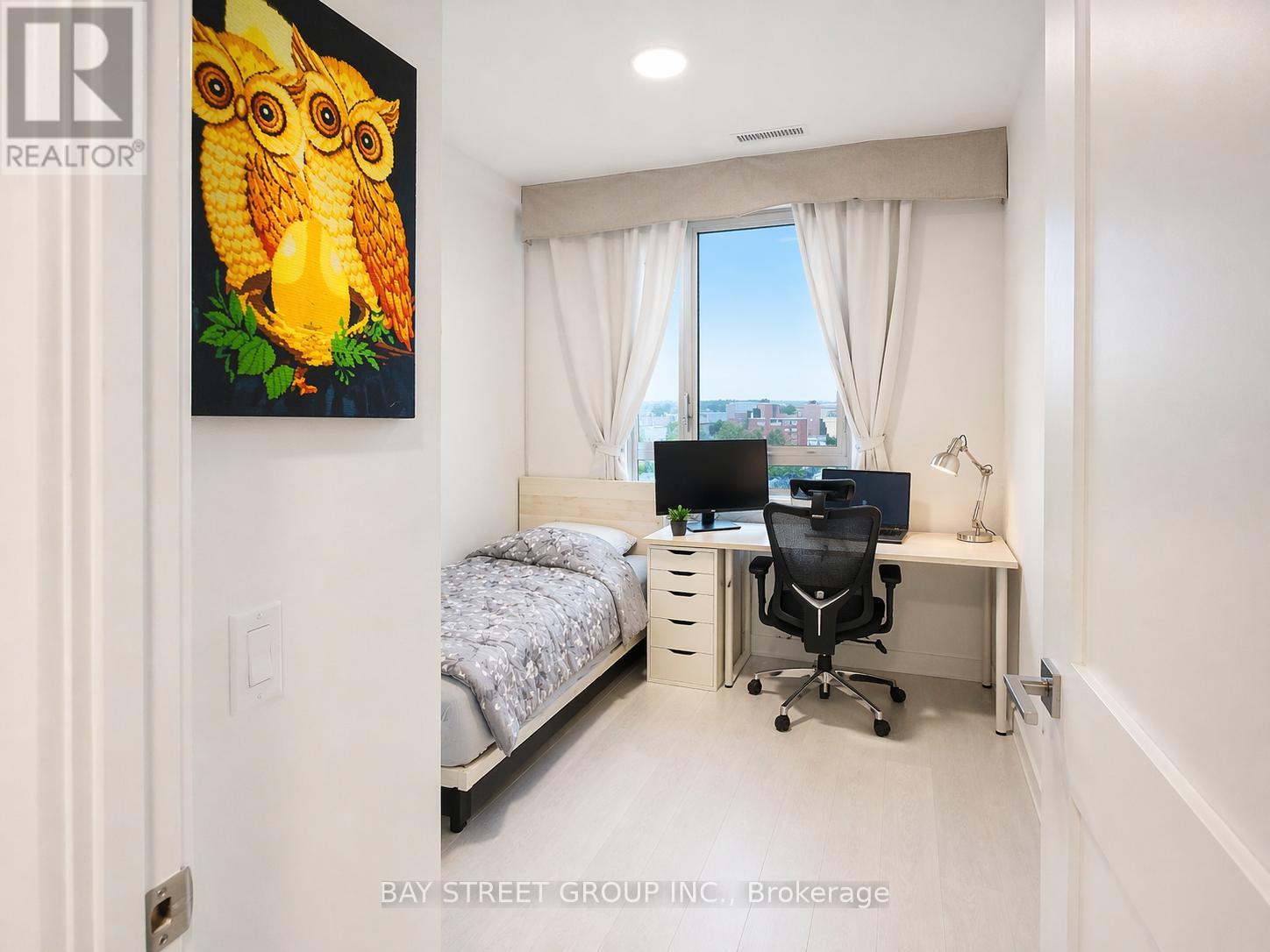 A bedroom with a bed, desk, and a painting of an owl.