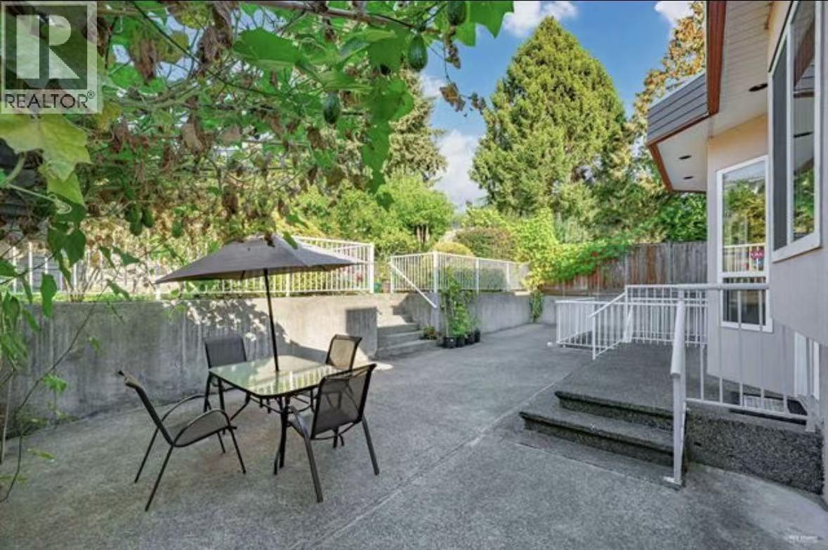 A patio with a table and chairs is surrounded by greenery.