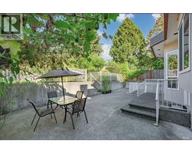 A patio with a table and chairs is surrounded by greenery.