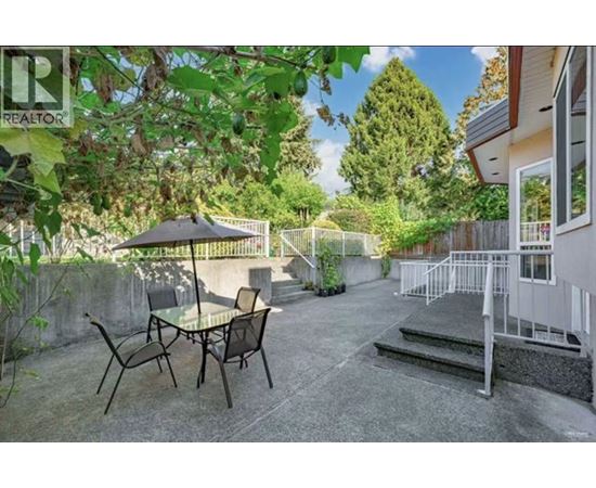A patio with a table and chairs is surrounded by greenery.