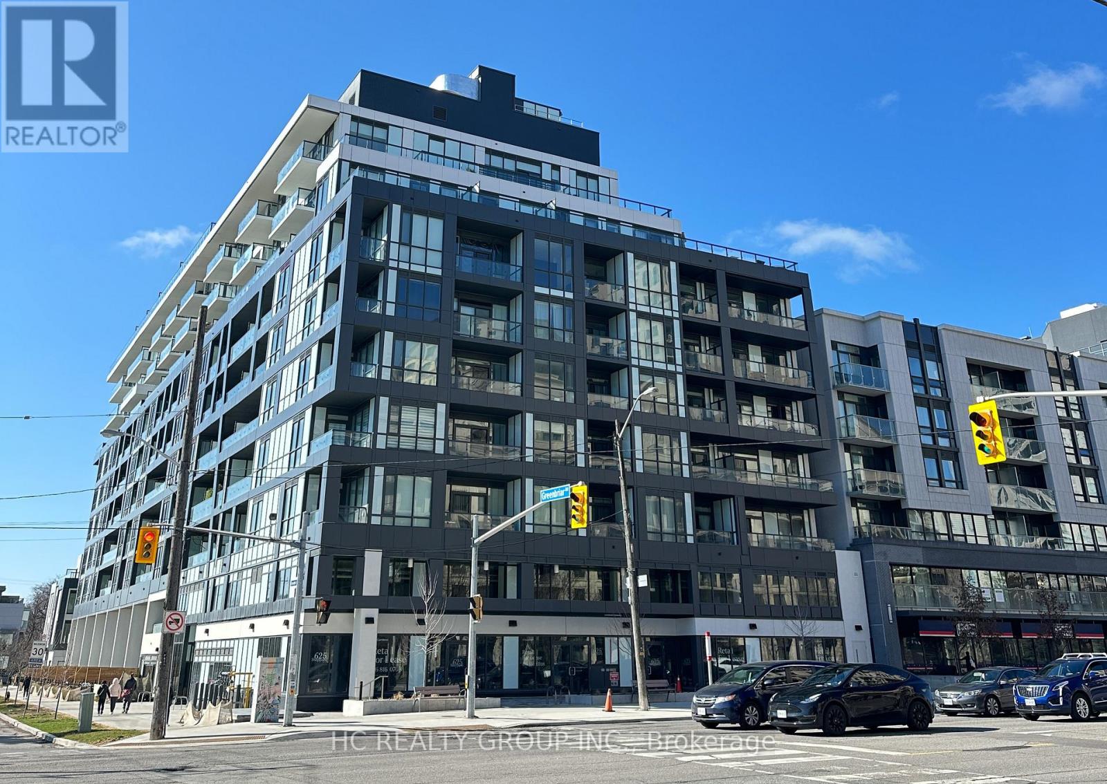 A modern multi-story building with a glass facade and a street view in front.