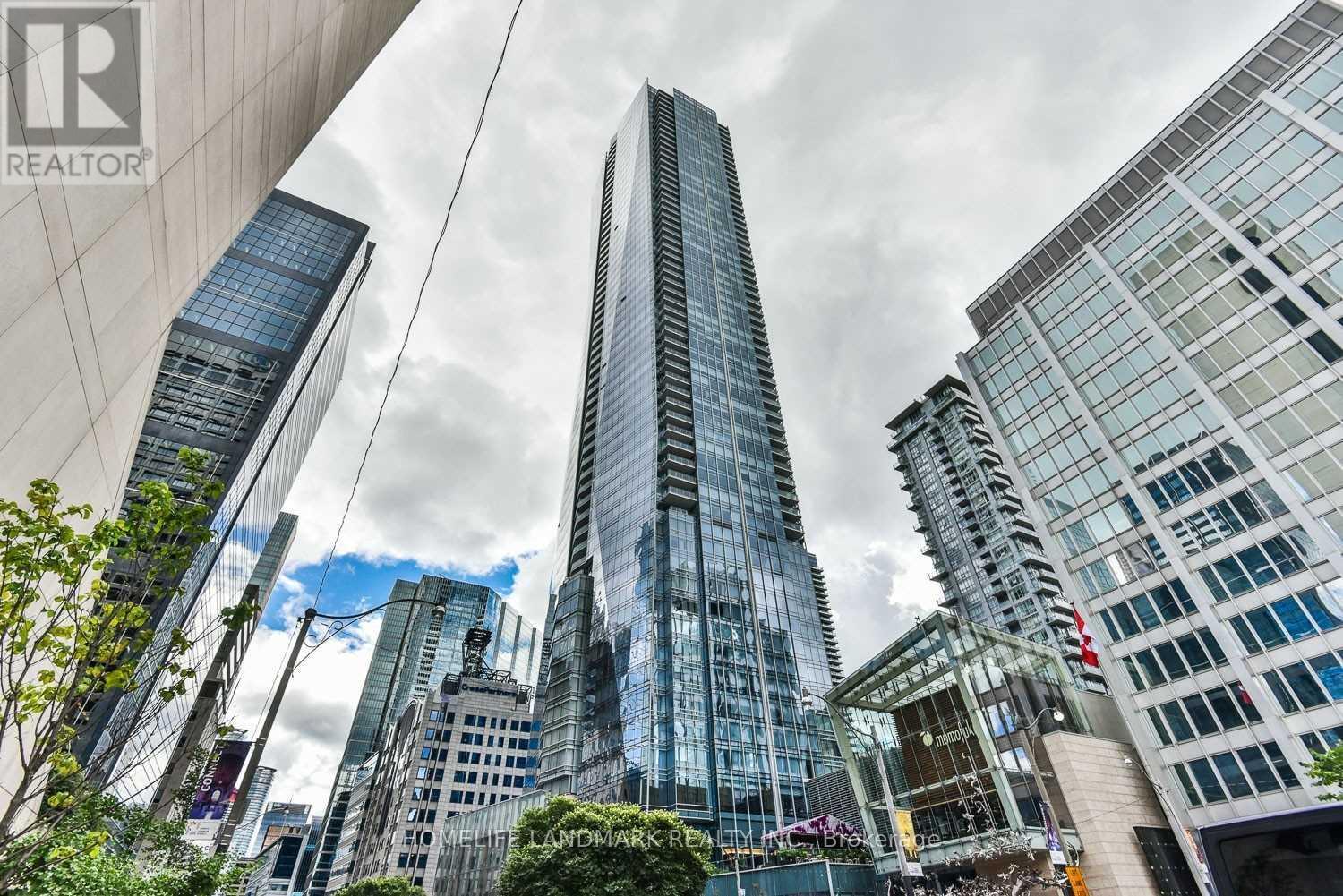 A cityscape with a tall building in the center and a realtor logo in the corner.