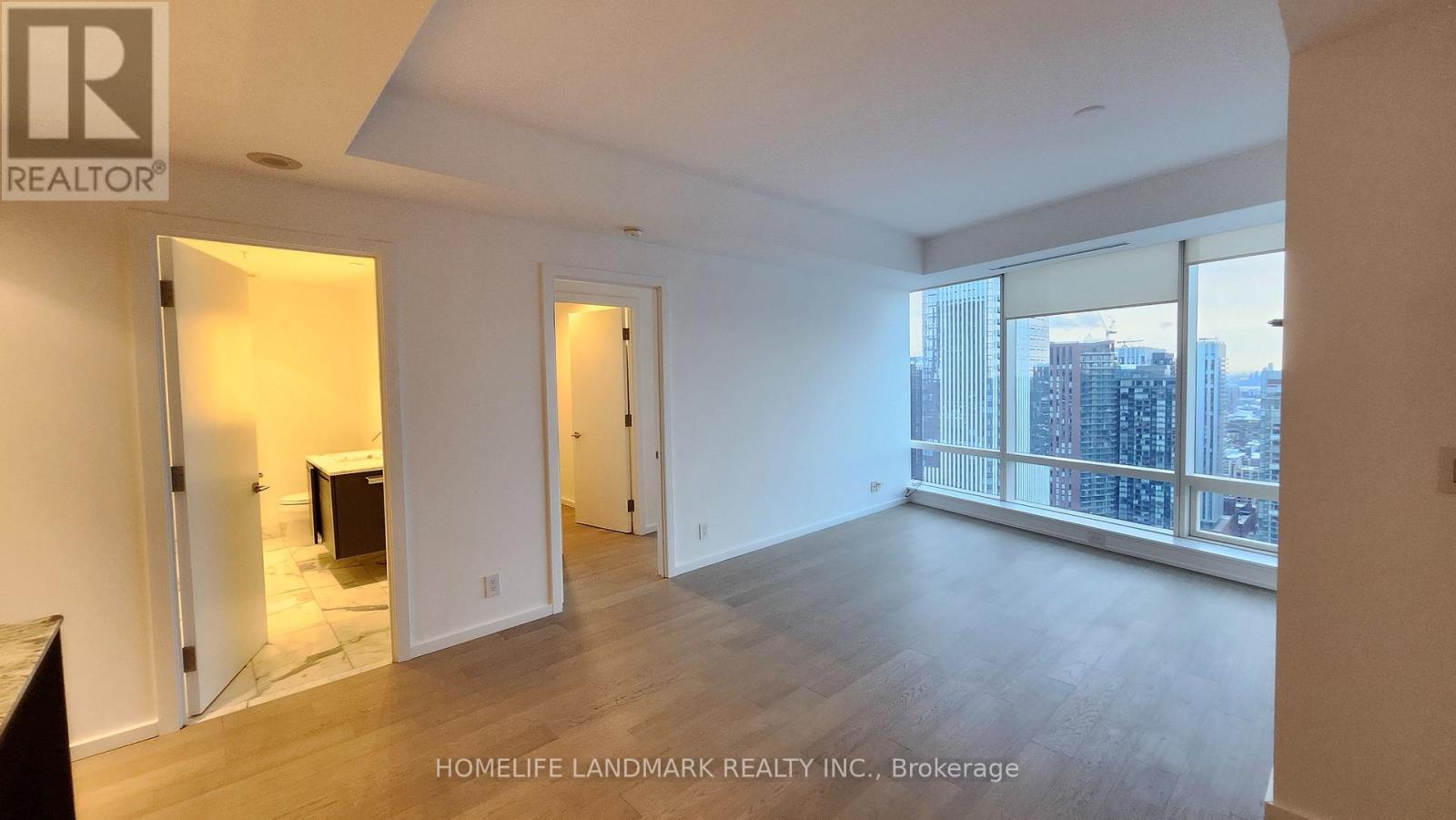 A spacious room with wooden floors and a large window overlooking a cityscape.