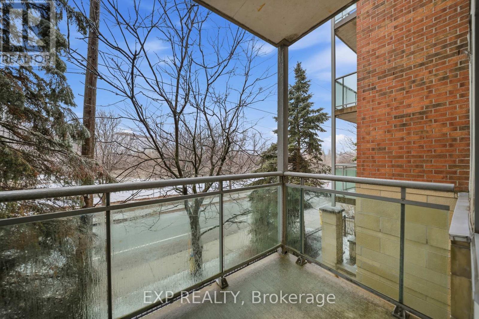 A balcony with a glass railing and a view of trees and a building.