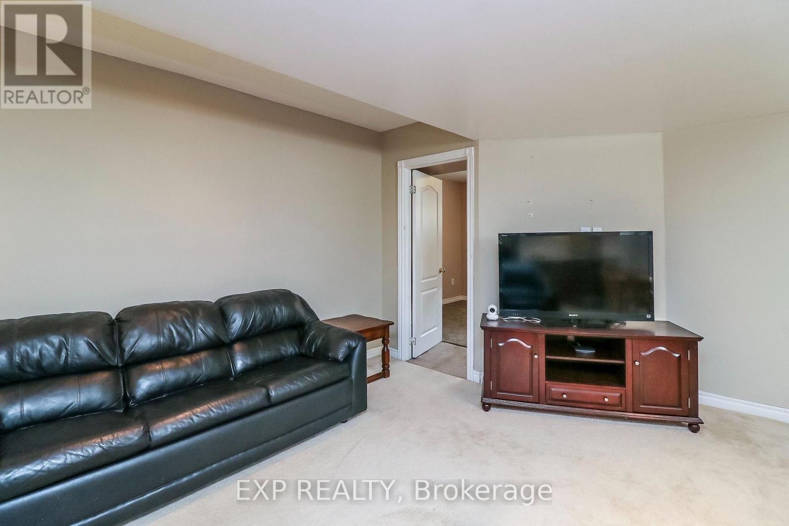A black leather couch sits in a living room with a wooden entertainment center and a flat screen TV.