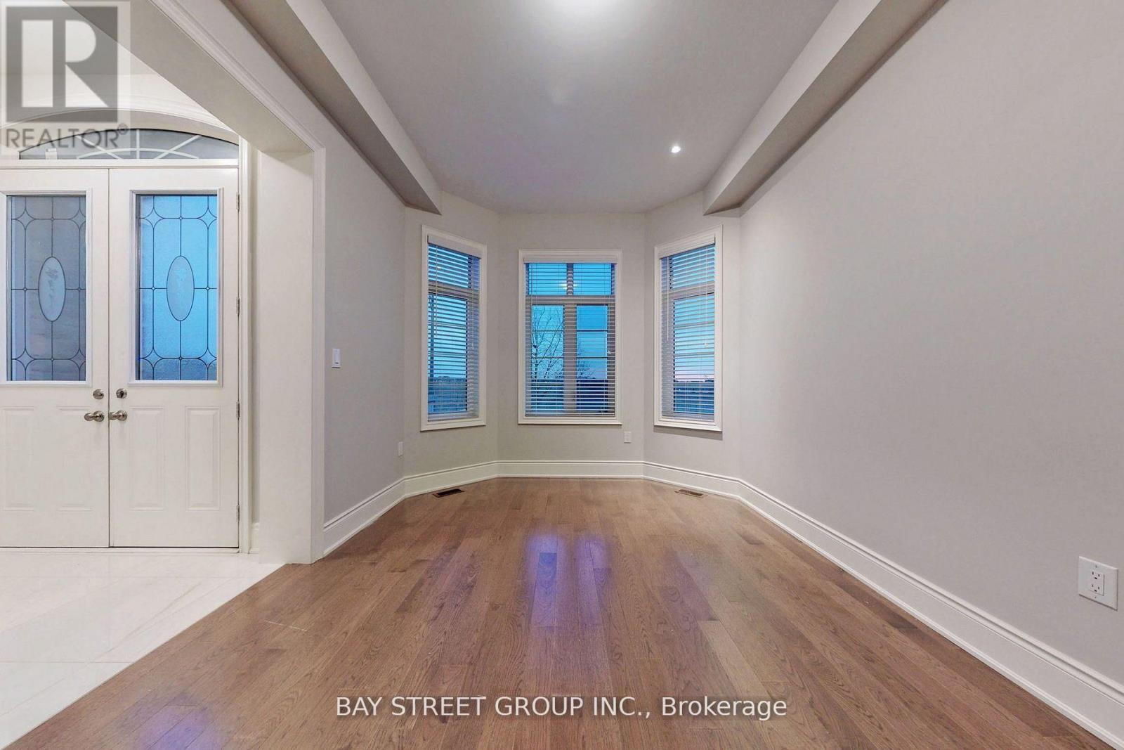 A spacious room with wooden floors and white walls, featuring a door with a glass panel and a window with blinds.