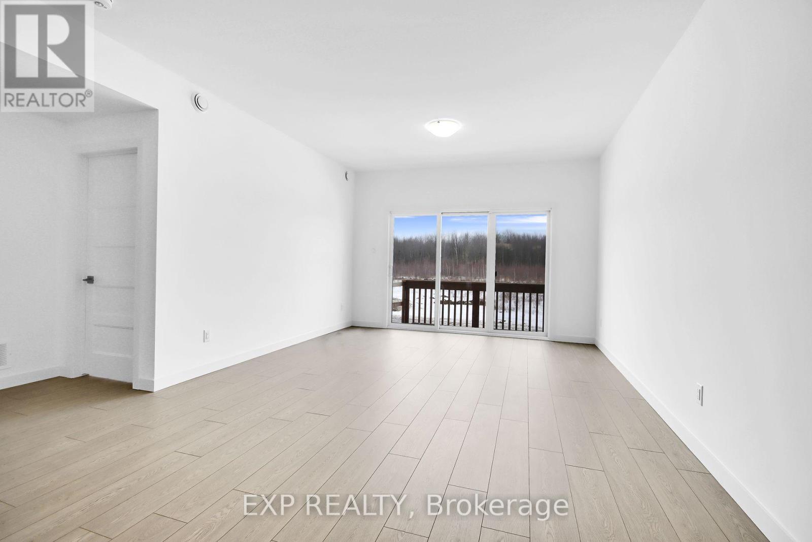 A spacious room with wooden flooring and a view of a deck through a sliding glass door.