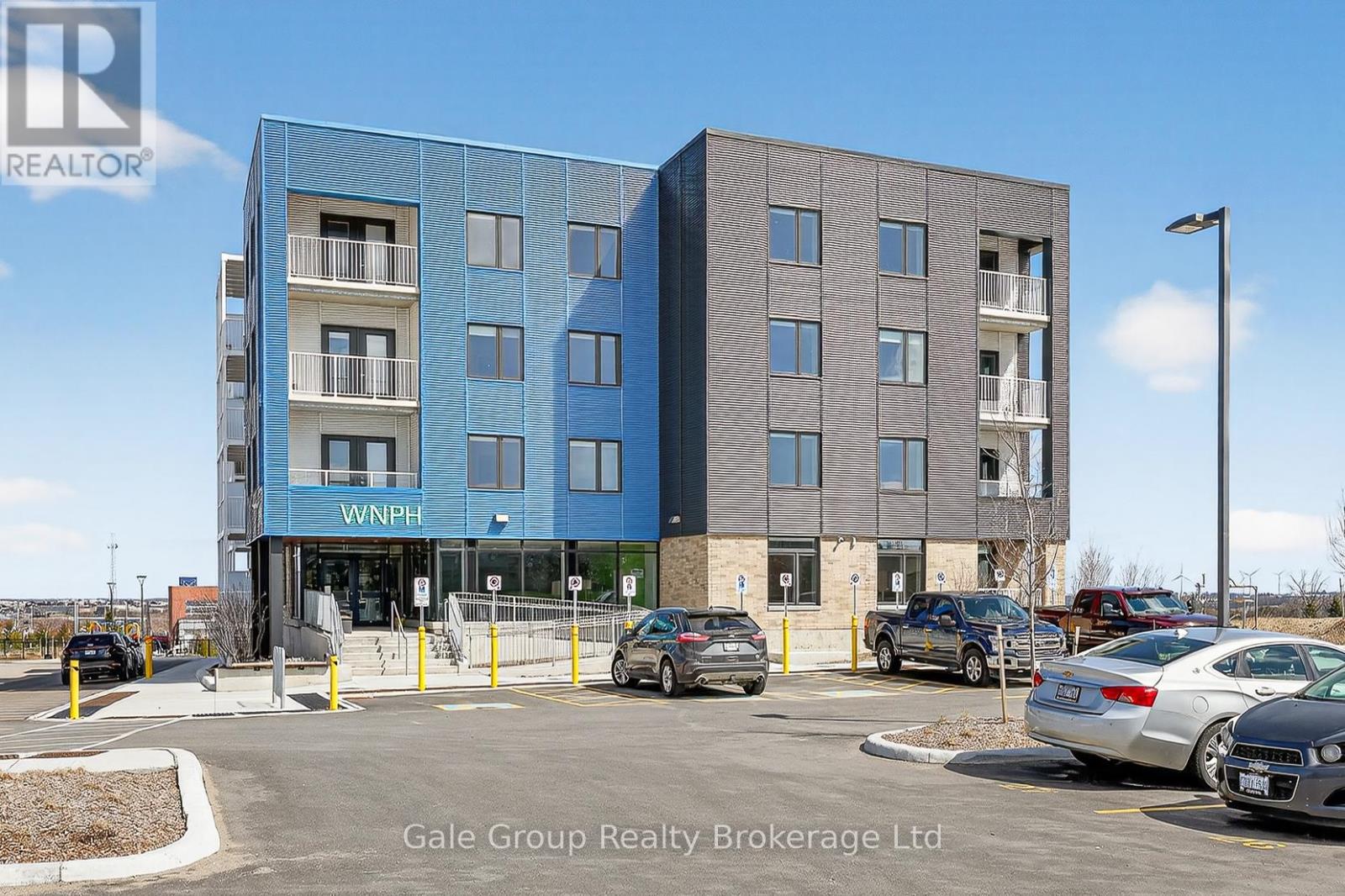 A modern two-story building with a blue and gray facade and a parking lot in front.