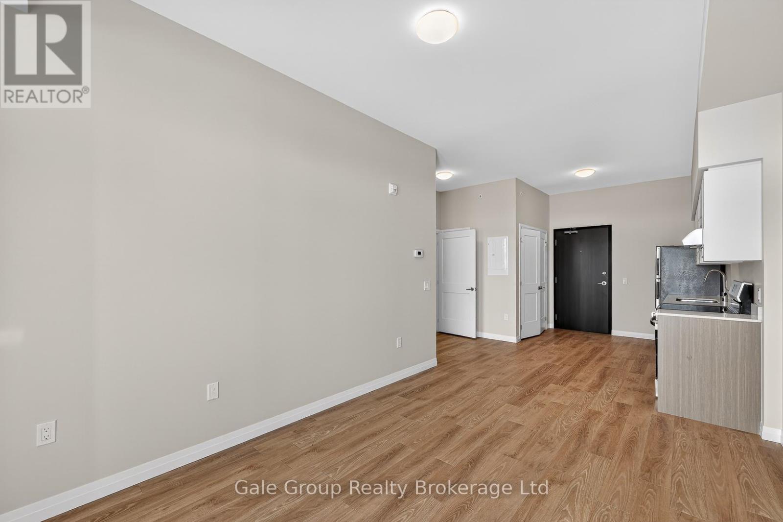 A spacious room with wooden flooring and a kitchenette area.