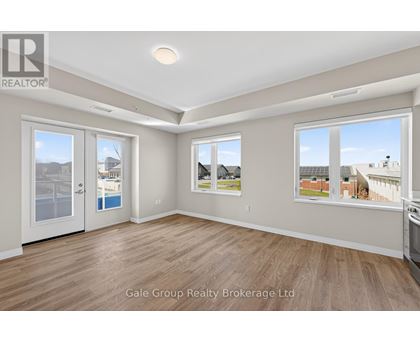 A spacious room with wooden flooring and large windows showing a view of other buildings.