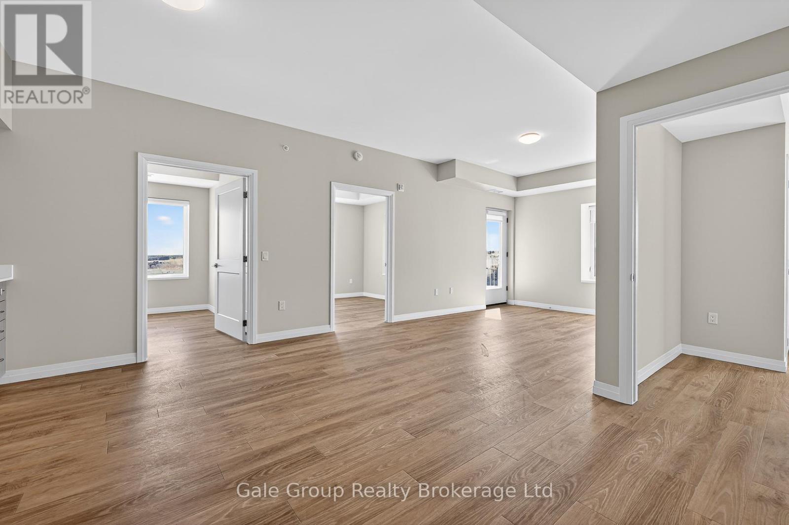 A spacious room with wooden flooring and white walls, part of a real estate brokerage.