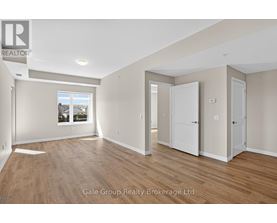 A spacious room with wooden flooring and white walls, with a window showing a view of trees and houses.