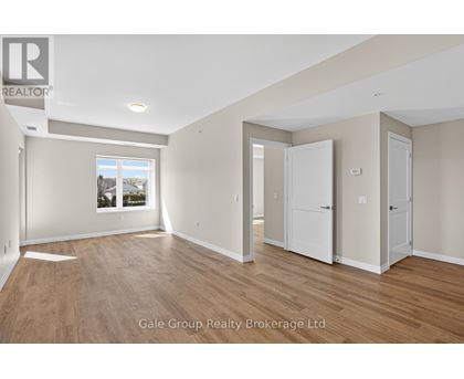A spacious room with wooden flooring and white walls, with a window showing a view of trees and houses.