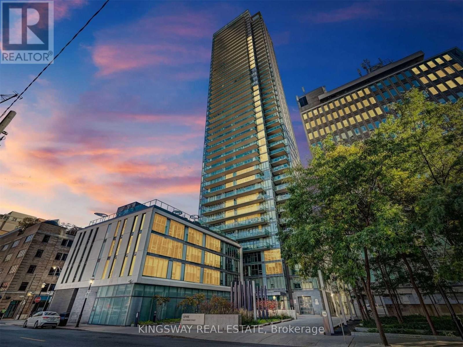 A tall building with a glass facade stands in front of a tree-lined street.