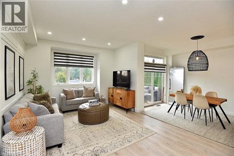 A living room with a grey couch, a brown ottoman, a wooden cabinet, a television, and a dining table with chairs.