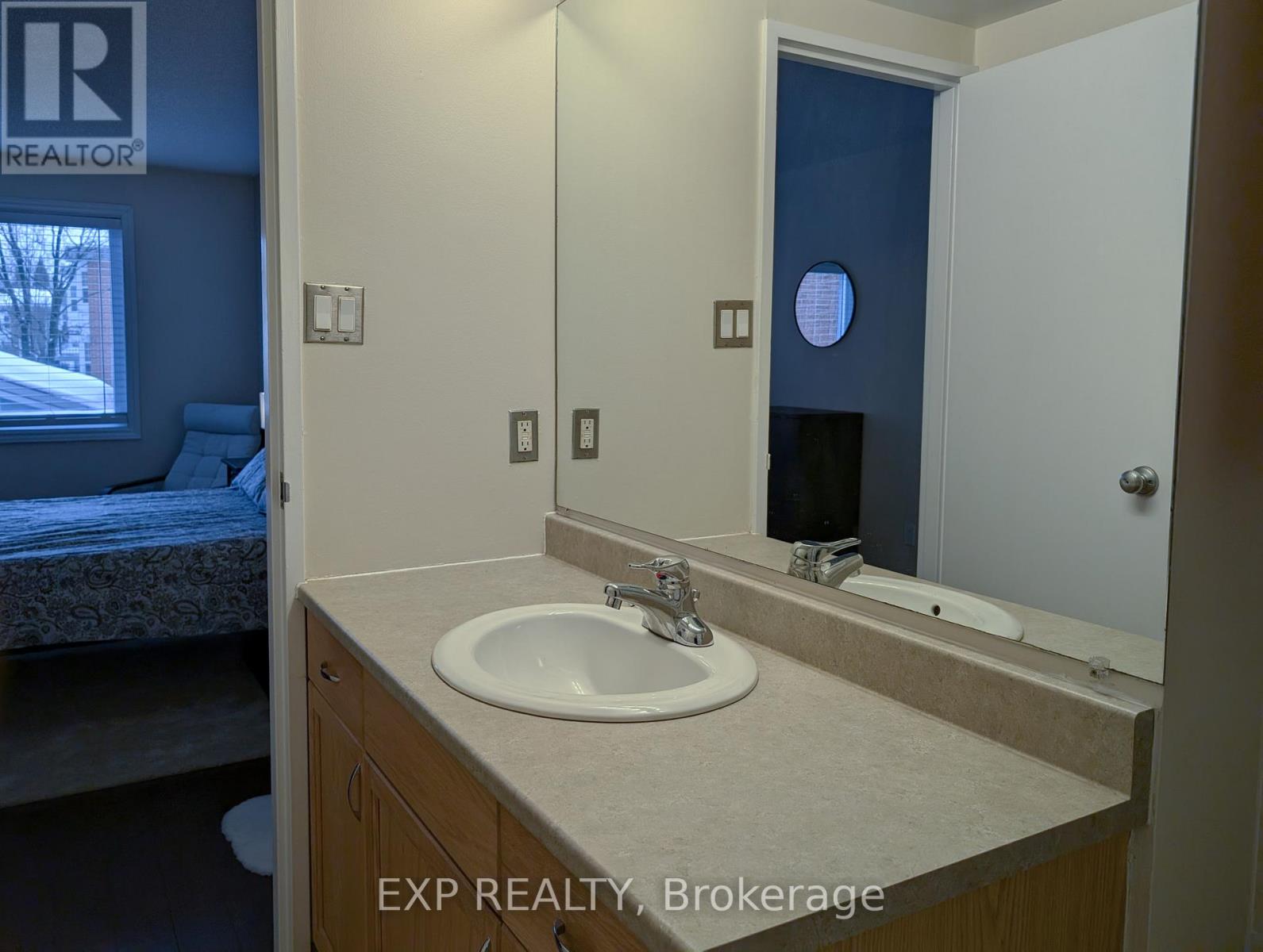 A bathroom with a sink, mirror, and a bedroom with a bed and window.