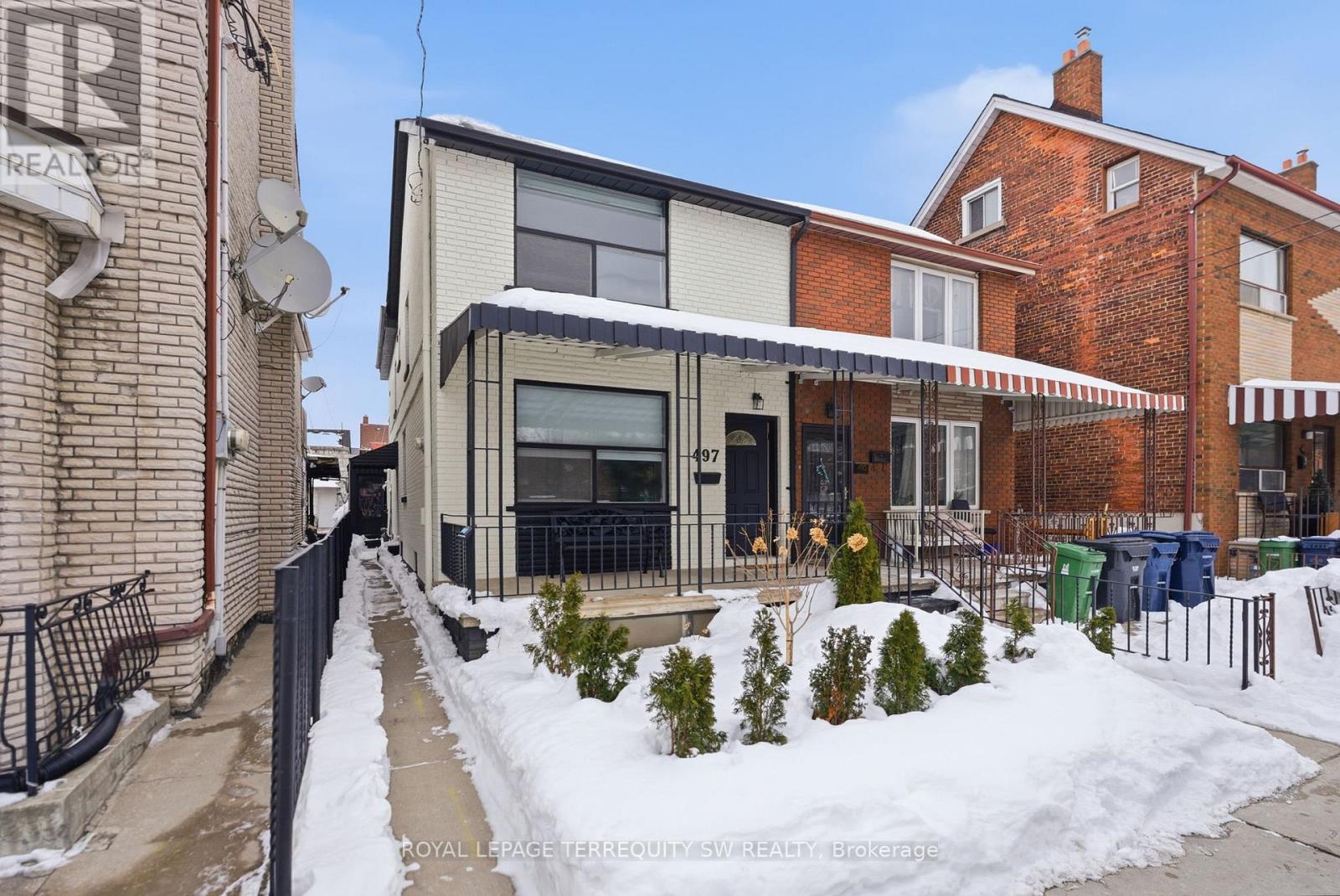 A snow-covered sidewalk leads to a modern building with a glass entrance.