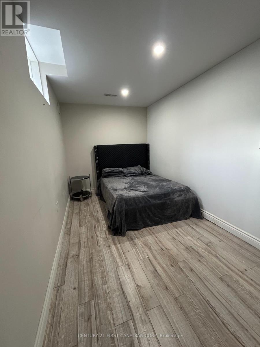 A bedroom with a bed covered in a grey sheet and a wooden floor.