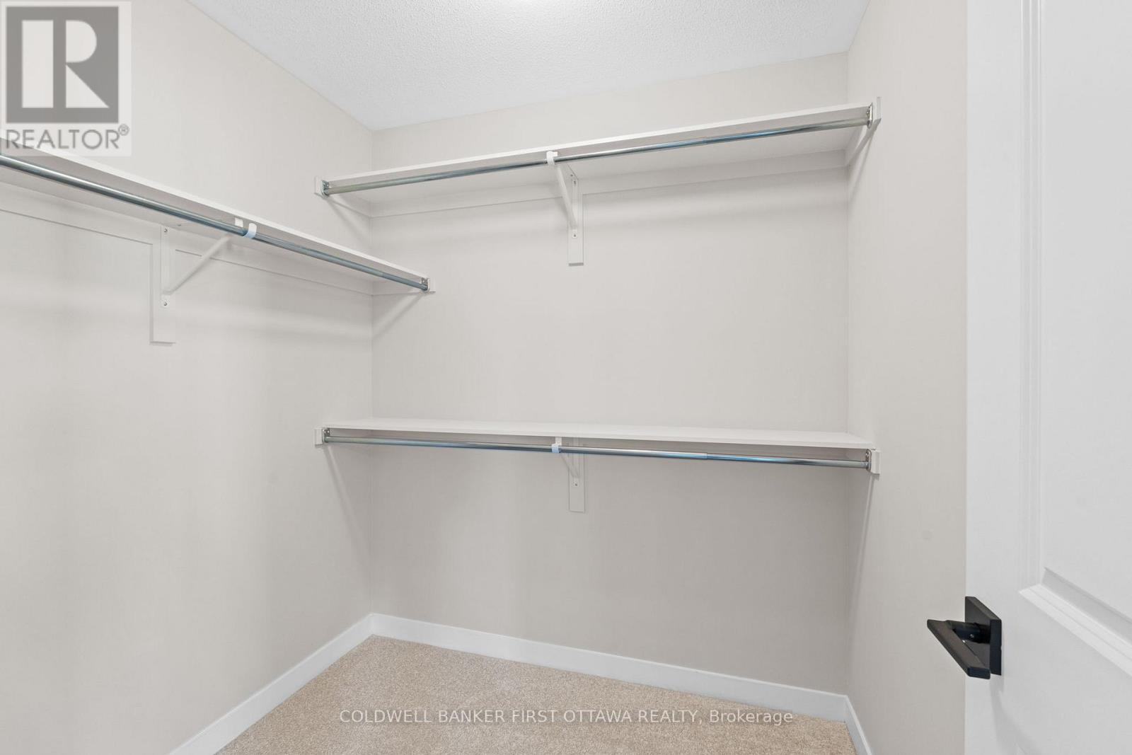A white bedroom with a bed frame and a brokerage sign.
