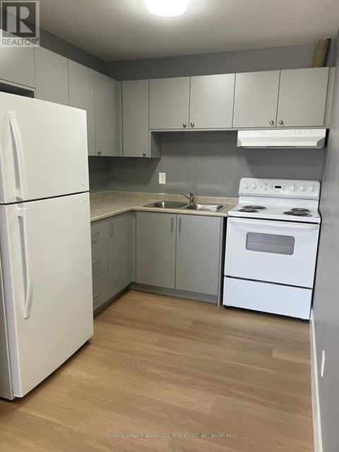 A white refrigerator is in a kitchen with wooden floors and white appliances.