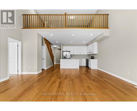 A spacious living room with wood flooring and a staircase with wooden railings.