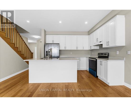 A modern kitchen with white cabinets and a wooden staircase.
