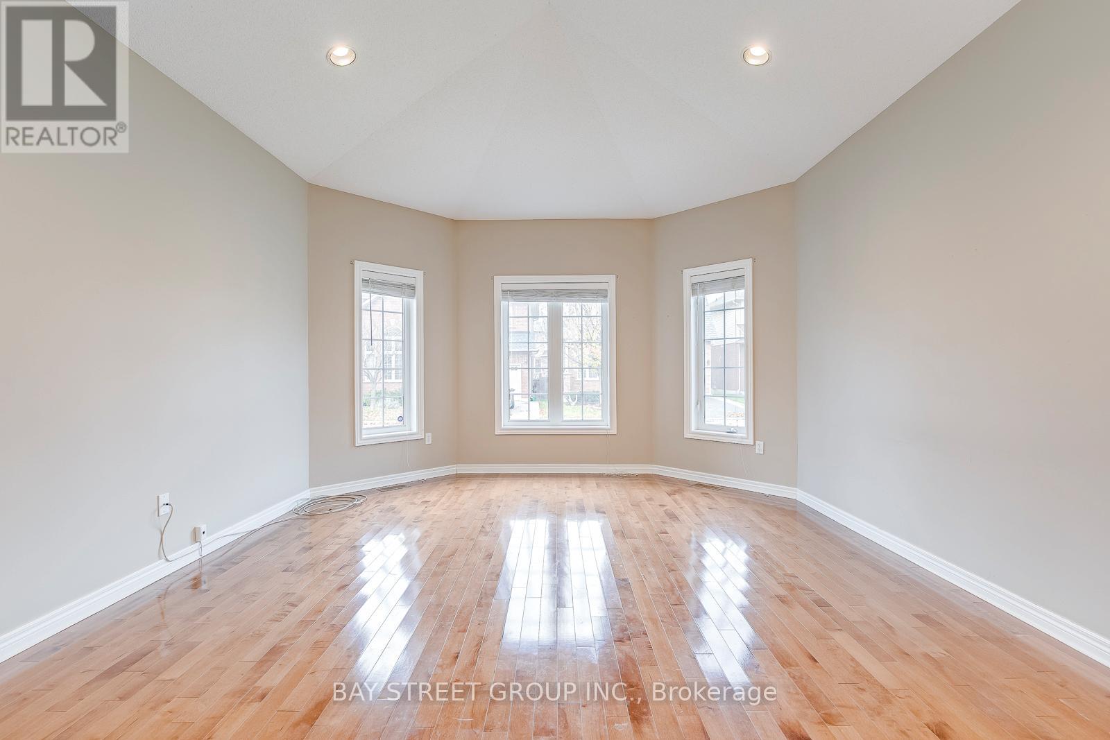 A spacious room with wooden floors and three windows.