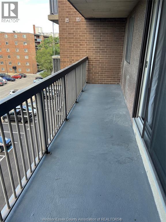 A balcony with a metal railing and a brick building in the background.