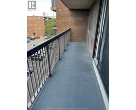A balcony with a metal railing and a brick building in the background.