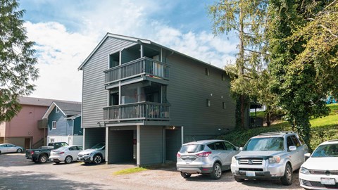 A grey two-story apartment building with a balcony and a garage door.