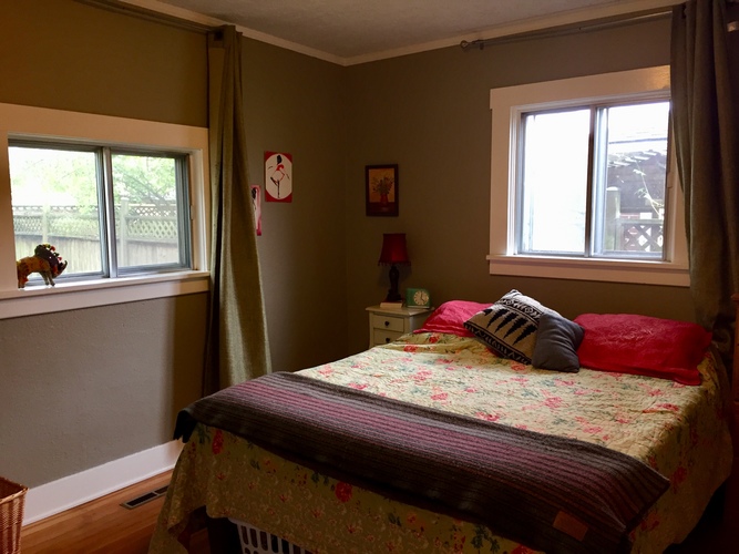 A bedroom with a bed, nightstand, window, and a small table with a lamp.