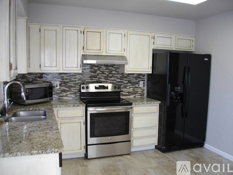 A kitchen with a black refrigerator and a stone backsplash.