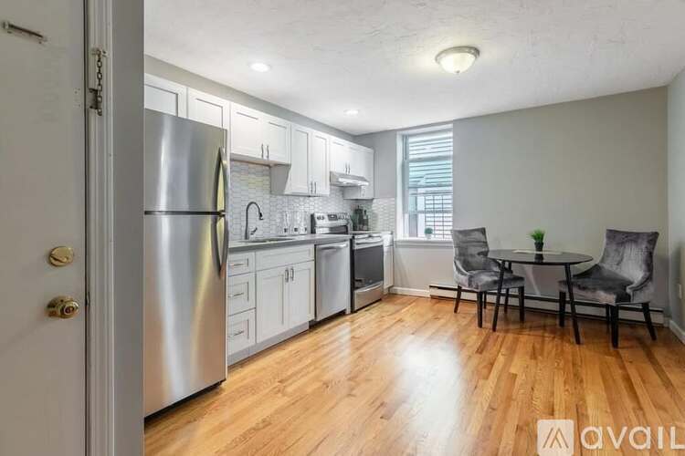 A kitchen with a refrigerator, sink, and a dining table with chairs.
