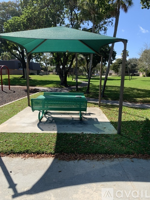 A green canopy is over a bench in a park.