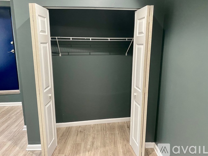 A white door is open to reveal a dark closet with a shelf and a wire hanger.