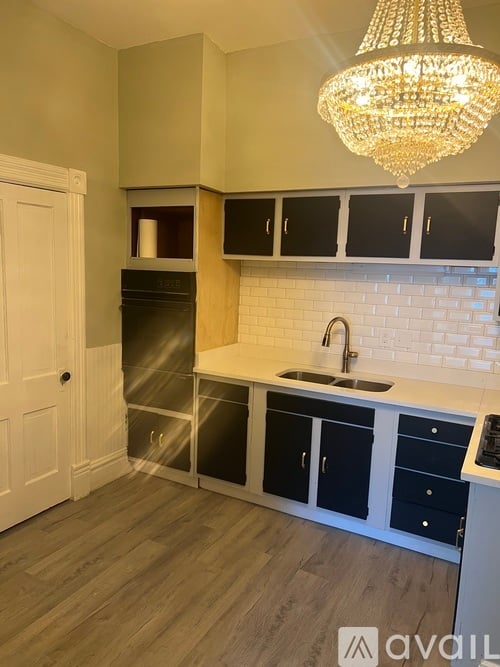 A kitchen with a white door, black cabinets, and a chandelier.