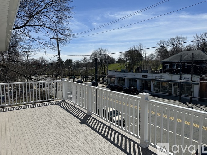 A white fence on a deck with a building and trees in the background.