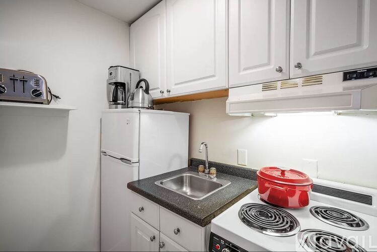 A white kitchen with a red pot on the stove.