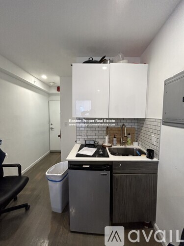 A kitchen with a sink, trash can, and a chair.