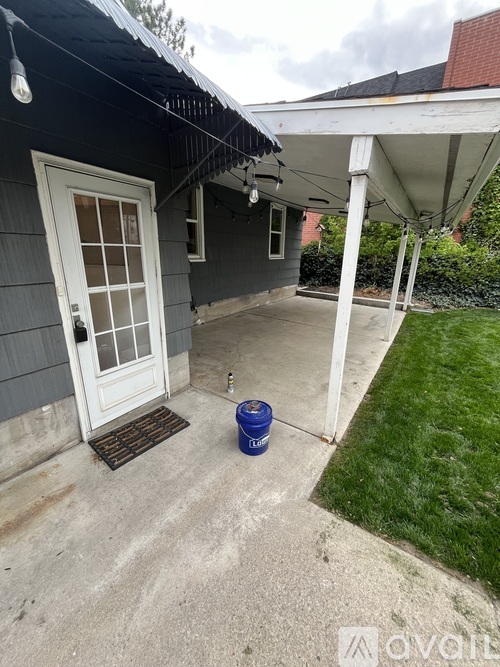 A blue bucket is on the concrete patio of a house.