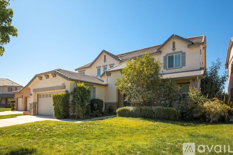 A large, two-story house with a garage is surrounded by a well-manicured lawn.