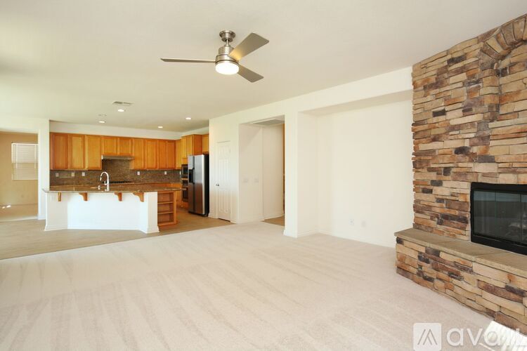 A spacious living room with a stone fireplace and a ceiling fan.