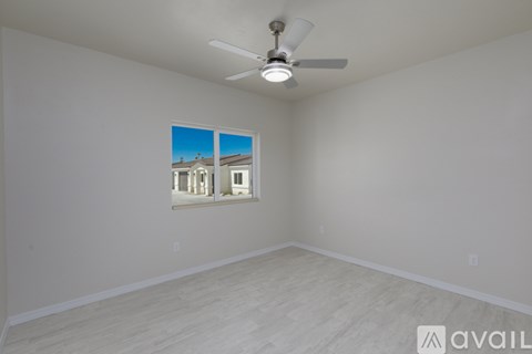 A room with a ceiling fan and a window showing a view of a building.