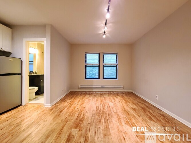 A spacious room with wooden flooring and a window with blinds.